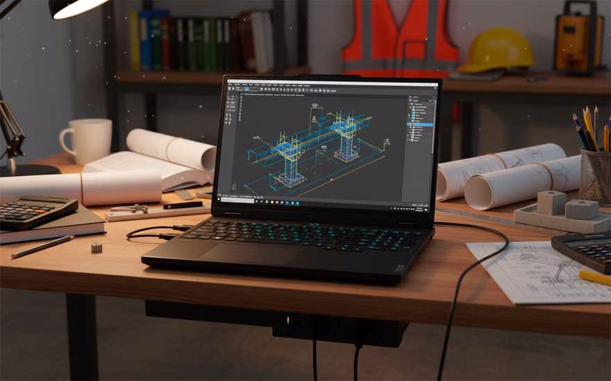 Laptop Lenovo Legion 5 mostrando AutoCAD en una mesa de trabajo de ingeniero civil, conectada a la toma de corriente. 